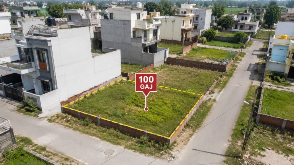 Aerial view of a marked 100 Gaj residential corner plot in a developed colony of Rudrapur, surrounded by independent houses and paved roads.