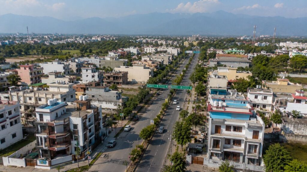 Aerial view of a modern residential area with 2 BHK flats and wide roads in Rudrapur, Uttarakhand, surrounded by greenery and mountain views.