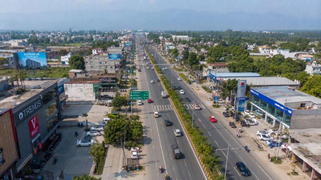 Aerial view of Kashipur Road in Rudrapur, Uttarakhand, showing commercial establishments, wide highway, and nearby residential developments ideal for property investment.